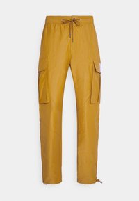 Nákladní kalhoty v hořčicově žluté barvě, s pasem na stažení na šňůrku, dvěma bočními kapsami a zúženými nohavicemi s úpravou u kotníků.