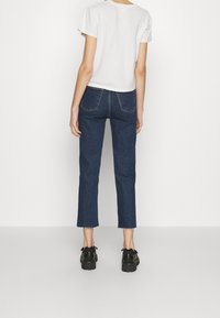 T-shirt bianco corto, jeans in denim blu scuro slim-fit con orlo sfilacciato e scarpe platform nere. Design semplice, senza motivi o accenti visibili.
