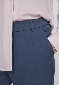 Pantalon bleu marine avec une texture lisse et une coupe fuselée. Associé à un chemisier rose clair avec un léger éclat et un col à boutons.
