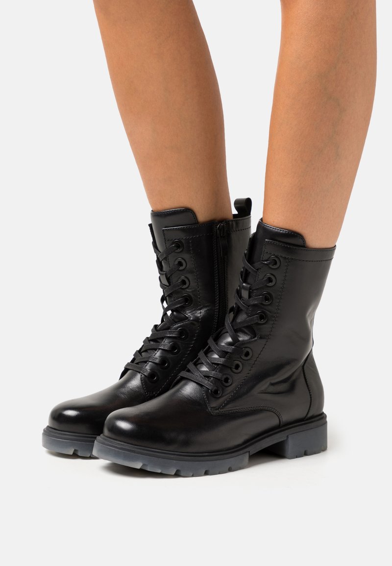 Botas de cuero negro hasta el tobillo con cordones en la parte frontal, cremallera lateral y suela de goma gris. Presentan una textura suave y un diseño de punta redonda.