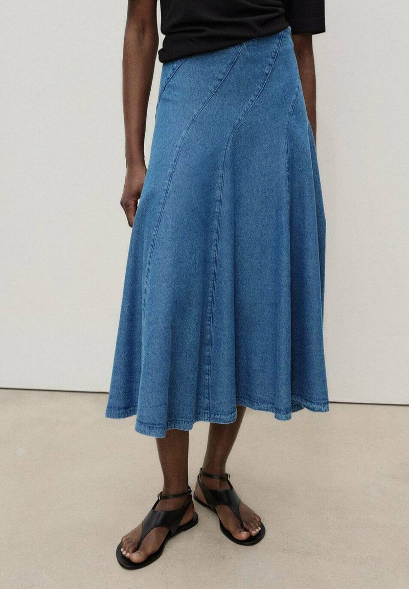 Jupe en denim bleu clair, de forme évasée, avec des coutures courbes et un ourlet fluide. Assortie à des sandales plates noires, au design à lanières.