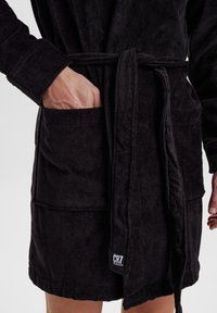 Black terry cloth bathrobe with a belted waist, featuring a patch pocket and textured fabric. Logo tag visible near hem.