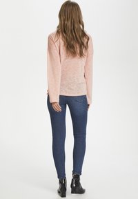 Jasnoróżowa koszula z długim rękawem, wykonana z lekkiego materiału, luźny krój. Połączona z ciemnoniebieskimi wąskimi dżinsami i czarnymi botkami za kostkę.