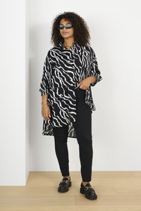 Chemise rayée en noir et blanc avec une coupe ample, des manches longues et des fentes sur les côtés, associée à un pantalon skinny noir et des chaussures noires épaisses.
