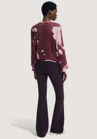 Sweter dzianinowy w burgundzie z różowymi wzorami tie-dye, długimi rękawami i luźnym krojem, zestawiony z dzwonowymi ciemnofioletowymi dżinsami.