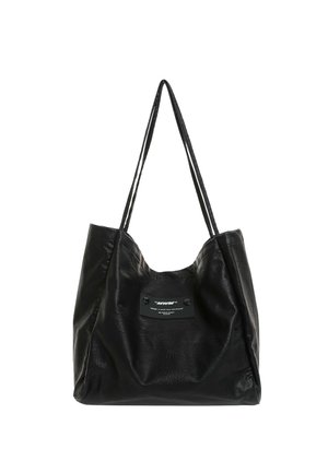 Bolso tote de cuero negro con asas largas y un pequeño parche rectangular con texto blanco en el centro delantero.
