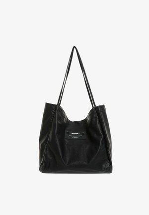Bolso tote de cuero negro con asas largas y un pequeño parche rectangular con texto blanco en el centro delantero.