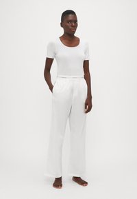 Weißes kurzärmliges Oberteil mit Rundhalsausschnitt, kombiniert mit locker sitzenden weißen Hosen mit elastischem Bund und markantem Akzent. Glatte Textur.