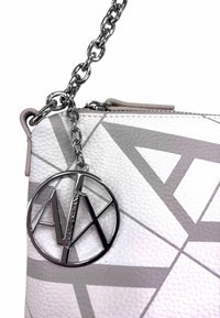 Borsa a tracolla in pelle bianca con texture, caratterizzata da motivi geometrici grigi, una tracolla in catena argentata e un ciondolo con logo metallico. Chiusura superiore con zip.