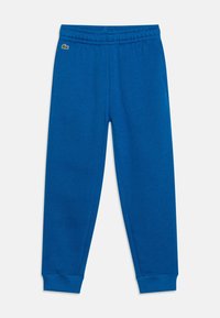 Blå fleecebyxor med elastisk midja, uppvikta fållar och sidofickor. Har en liten grön logotyp på framsidan.