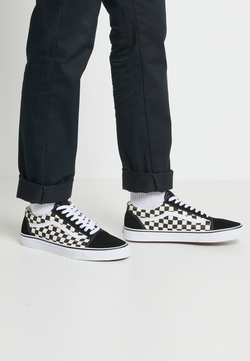 Sorte og hvide ternede kanvas sneakers med hvide snørebånd, sorte accenter og gummisål, parret med marineblå bukser.