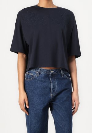 Navy cropped t-shirt with short sleeves, featuring textured floral embroidery on the chest, paired with high-waisted blue denim jeans.