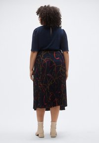 Tengerészkék felső rövid fodros ujjakkal, hozzá egy pliszírozott fekete szoknya piros és arany színű lánc- és szalagmintával. B�ézs bokacsizma.