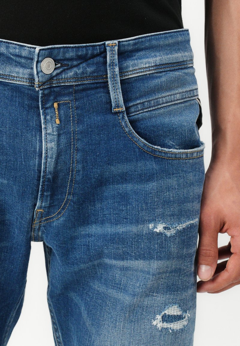 Jeans de mezclilla azul deslavado con un corte recto, que presentan detalles de costura, bolsillos frontales y áreas desgastadas cerca de las rodillas.