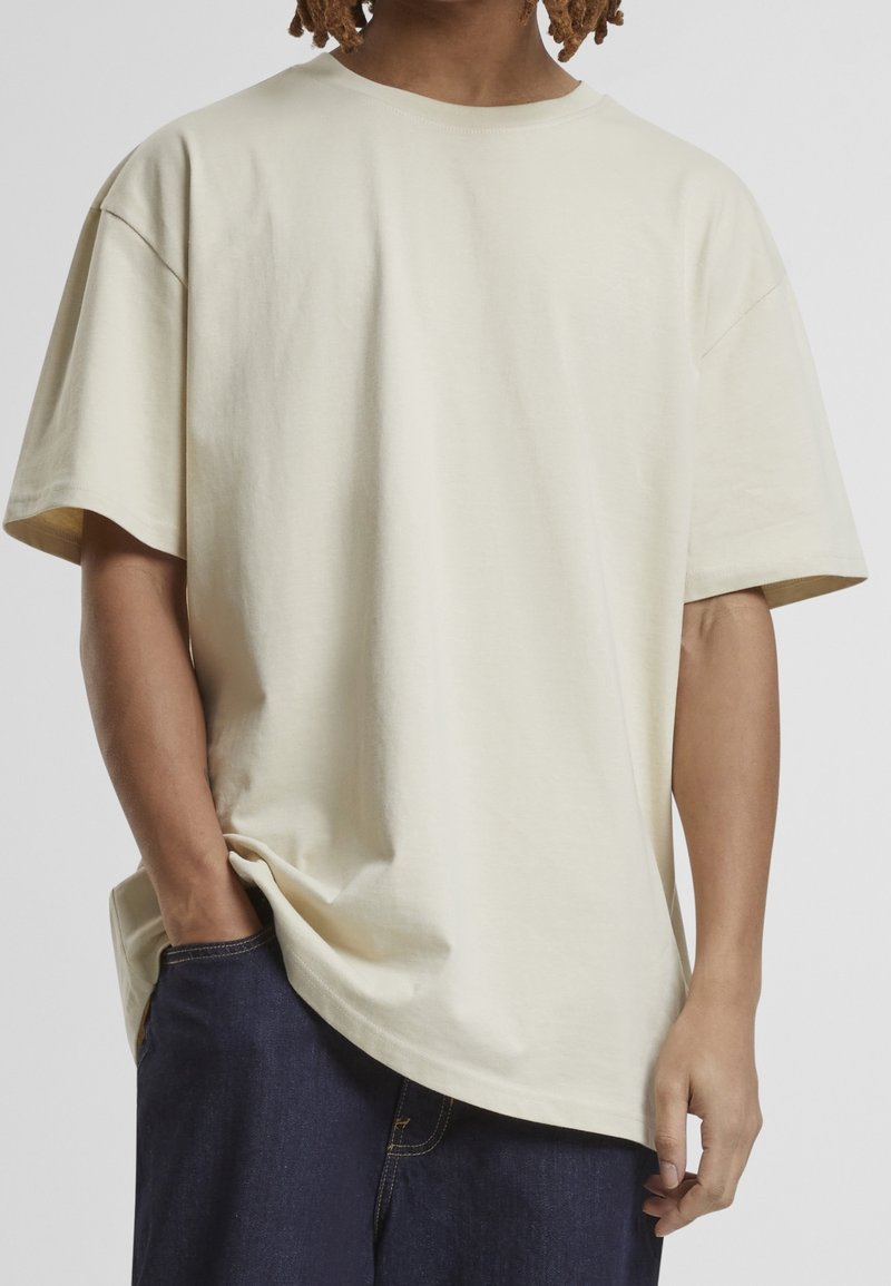 T-shirt à manches courtes couleur crème en tissu doux, avec une coupe décontractée et un col rond, associé à un short en denim bleu foncé.