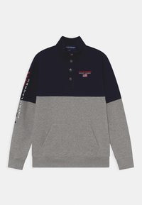 Marinblå och grå sweatshirt med krage, tre knappar, främre ficka och sidotryckta logodetaljer i röd och vit. Mjuk materialkänsla.