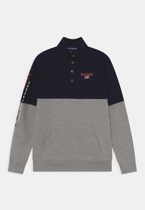 Sweatshirt bleu marine et gris avec un col, trois boutons, poche avant et détails de logo imprimés sur le côté en rouge et blanc. Texture de matériau douce.