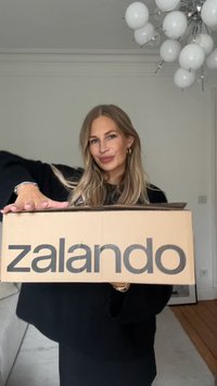 Hnědá kartonová krabice s nápisem "zalando" vytištěným velkým černým písmem. Krabice je držená osobou oblečenou v černém, s plochým okrajem nahoře.