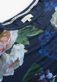 Marineblauwe bloemen top met grote rozen- en pioenrozenprints in roze, wit en blauw. Zachte stof met een ronde halslijn. Label zichtbaar.