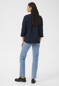 Camicia blu navy a trama con maniche a tre quarti, abbinata a jeans azzurri e scarpe nere slip-on. Design posteriore semplice, senza motivi visibili.