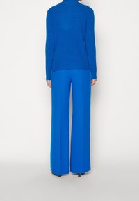 Pull à col roulé côtelé bleu associé à un pantalon large bleu. Texture lisse, haut moulant et pantalon long et fluide créent un look harmonieux.