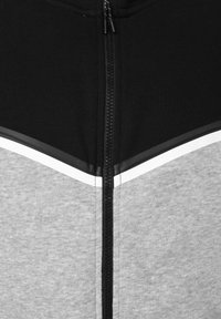 Μαύρο και γκρι μπουφάν με φερμουάρ μπροστά και λευκή επένδυση, που δείχνει την περιοχή του άνω στήθους και του γιακά με λεπτομέρειες ραφής.