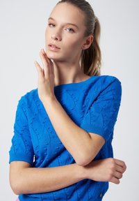 Suéter de punto azul con un diseño texturizado y patrones en relieve, mangas cortas y cuello redondo, que resalta un acabado suave.