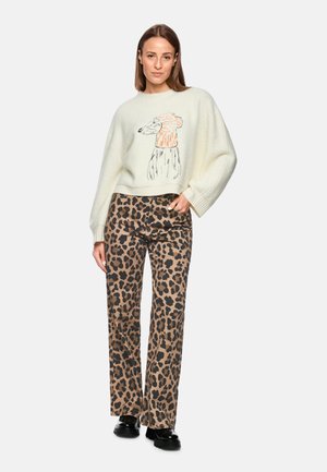 Cream oversized sweater with an orange and black illustration, paired with brown leopard print wide-leg pants and black platform shoes.