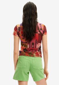 Camiseta ajustada multicolor con patrones florales, combinada con pantalones cortos de denim verdes de cintura alta que cuentan con dos bolsillos traseros y un acabado texturizado.