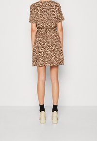Hnědé krátké šaty s leopardím potiskem, krátkými rukávy a úzkým pasem, doplněné béžovými botami na blokovém podpatku a černými ponožkami.