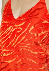 Top de cetim vermelho com decote em V e padrão texturizado de riscas de zebra em dourado. O tecido parece suave com um leve brilho.