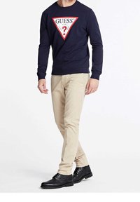 Sudadera navy con un logo gráfico triangular en rojo y blanco, pantalones beige y zapatos negros de cordones, todo sobre un fondo sencillo.