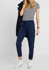 Námořnické modré tepláky s elastickým pasem a stahovací šňůrkou, s náprsní kapsou, spárované s černobílým pruhovaným tričkem.