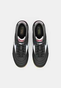 Pantofi sport din piele neagră cu accente albe, suprafață texturată, vârf rotund și talpă din gumă. Prezintă șireturi clasice și un logo pe limbă.