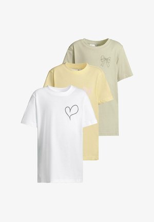 Világoszöld pamut póló, masni grafikával, fekete leggingsszel, színes virágmintákkal, és fekete cipővel párosítva.