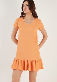 Short orange dress with a V-neck, short sleeves, textured fabric, and a frilled hem, offering a loose and comfortable fit.