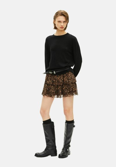 Jersey negro de manga larga, falda de leopardo con volantes, botas altas de cuero negro con hebillas y calcetines negros acanalados.