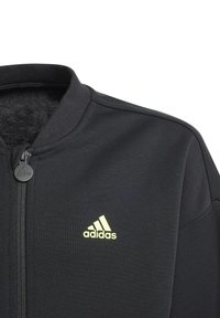 Giacca nera con zip realizzata in tessuto morbido. Presenta un colletto alto e un logo Adidas verde neon sul lato sinistro del petto.
