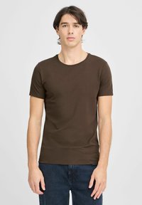 T-shirt marron à manches courtes en tissu doux, avec un col rond et une coupe slim, associé à un jean en denim bleu foncé.
