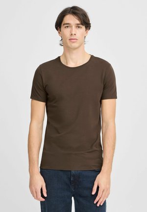 Tricou scurt cu mânecă, de culoare maro, dintr-un material moale, cu guler rotund și un design slim fit, purtat cu blugi de denim de culoare albastru închis.