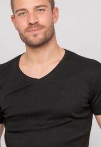 T-shirt noir à col en V fabriqué en tissu de coton lisse. Il présente un logo en relief discret sur la poitrine gauche et un design ajusté.