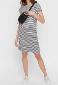 Czarna i biała sukienka w paski z krótkimi rękawami, do kolan, z miękkiego materiału. Noszona z czarną torebką typu crossbody i białymi butami slip-on.