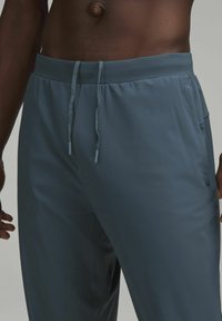 Herrbyxor i gråblått, tillverkade av lätt material, med elastisk midja och dragsko, sidofickor och slät yta.