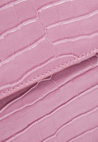 Finta pelle rosa con un motivo in pelle di coccodrillo presenta una finitura liscia e lucida con cuciture visibili. Design compatto con superficie texture.