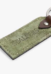 Llavero de ante verde con un acento de cuero marrón y herrajes de plata. Presenta texto en relieve y bordes cosidos para mayor durabilidad.