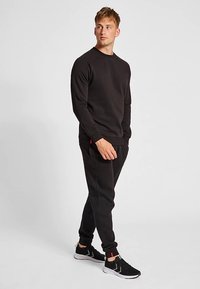 Sort sweatshirt og joggers i blødt stof med rund halsudskæring, lange ærmer, elastiske manchetter og tætsiddende pasform med diskrete røde detaljer.