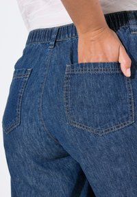 Vaqueros de denim de color azul medio, con una textura suave, cinturilla elástica y dos bolsillos traseros con bordes cosidos.