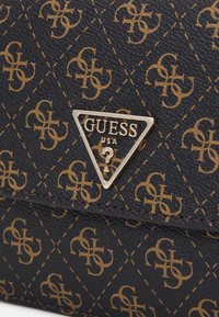 Zwarte gestructureerde synthetische handtas met een herhalend goudkleurig logo-patroon en een metalen driehoekig merkembleem met "GUESS USA."