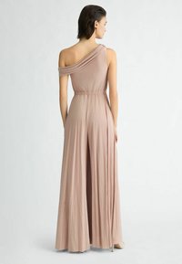 Eén-schouder, geplooide jumpsuit van zachte roze stof met een elastische tailleband en vloeiende wijde benen, voorzien van een subtiele glans en minimale hardware.