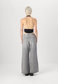 Črn halter top v kombinaciji z visokim pasom, širokimi svetlo sivimi kavbojkami. Kavbojke imajo blede zaključke in zadnje žepe.